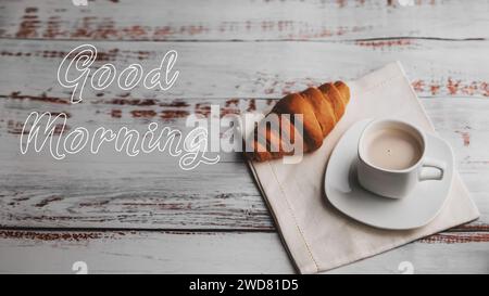 Carte de voeux avec l'inscription Good Morning. Une tasse de café et un croissant sur une table en bois blanc Banque D'Images