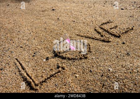 Amour intemporel : « l'amour » inscrit sur la plage, berçant un sablier rose, où la romance rencontre le sable des moments éternels Banque D'Images