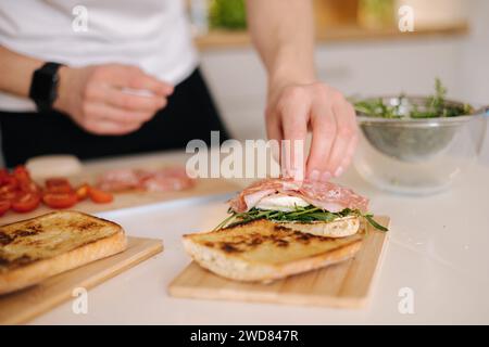 L'homme a mis une tranche de salami italien sur le dessus de bruschetta. Des aliments sains faits maison Banque D'Images