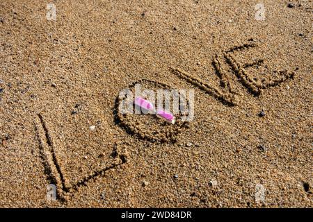 Amour intemporel : « l'amour » inscrit sur la plage, berçant un sablier rose, où la romance rencontre le sable des moments éternels. Banque D'Images