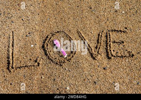 Amour intemporel : « l'amour » inscrit sur la plage, berçant un sablier rose, où la romance rencontre le sable des moments éternels Banque D'Images