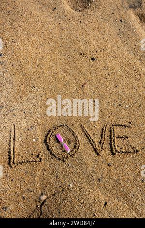 Amour intemporel : « l'amour » inscrit sur la plage, berçant un sablier rose, où la romance rencontre le sable des moments éternels. Banque D'Images