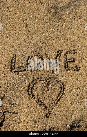 Lettre d'amour de bord de mer : 'amour' et coeur dessiné dans le sable, un tableau romantique gravé par les vagues Banque D'Images