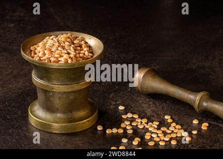 Un gros plan d'un mortier de bronze vintage et pilon avec des pois secs sur un fond sombre. Cette image évoque un conceps culinaire rustique et traditionnel Banque D'Images