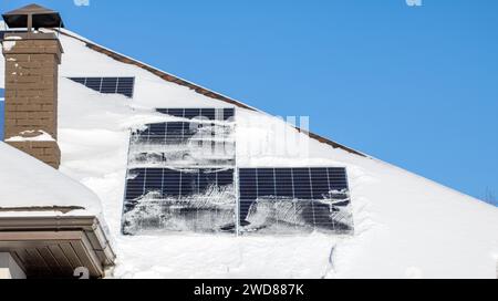 Toit avec panneaux solaires étant déneigé par une journée lumineuse avec un ciel bleu clair, montrant l'importance de maintenir les sources d'énergie renouvelables dans Banque D'Images