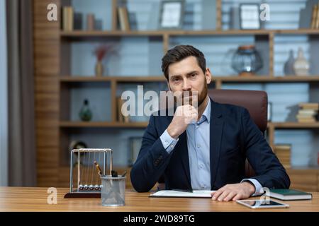 Un homme d'affaires mûr prêt reflète profondément tout en étant assis dans un bureau à domicile classique, exsudant professionnalisme et confiance. Banque D'Images