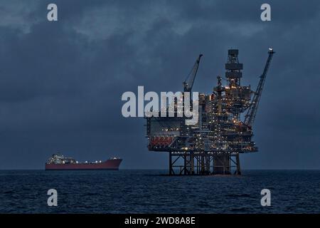 Production de pétrole brut en mer avec engin de forage à jackup et pétrolier de stockage de production flottant la nuit. Banque D'Images