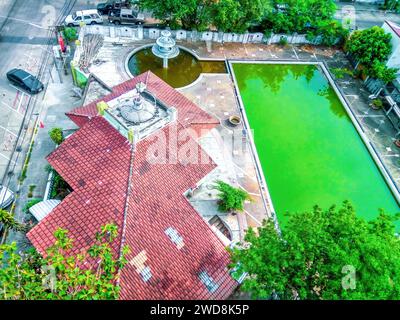 Maison avec toit en tuiles rouges, fontaine et piscine avec eau stagnante verte sale, vue de dessus. Abandonnez le vieux motel et la piscine rectangulaire avec stagnant Banque D'Images