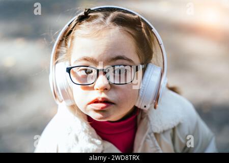 Gros plan portrait de belle petite fille dans des lunettes avec le syndrome de Down souriant et regardant dans la caméra avec l'expression faciale réfléchie. . Banque D'Images