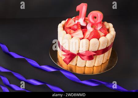 tarte aux fêtes d'anniversaire 18. gâteau de tiramisu aux fraises sur fond noir avec ruban doré et rouge.Concentrez-vous sur les fraises. Banque D'Images