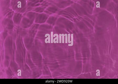 Texture de surface d'eau transparente rose transparente avec des ondulations, des vagues et des anneaux à la lumière du soleil. Fond aqua nature abstraite, reflets ensoleillés Banque D'Images