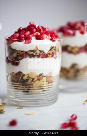 Parfait au yaourt en couches avec granola, graines et grenade fraîche dans le verre, petit déjeuner sain ou idée de collation. Banque D'Images
