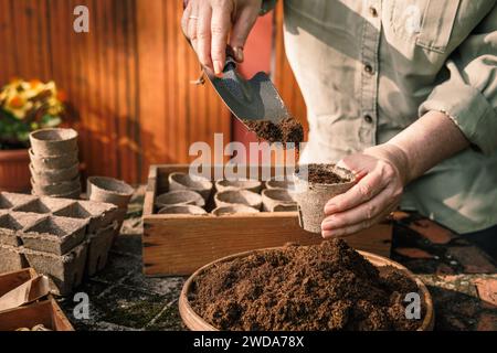 Jardinier avec pelle mettant la terre et le compost dans des pots de tourbe biodégradables. Planter et semer des graines. Jardinage printanier Banque D'Images