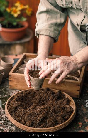 Jardinier mettant de la terre et du compost dans des pots de tourbe biodégradables. Plantation et semis au printemps Banque D'Images