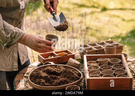Jardinage printanier. Jardinière féminine avec pelle mettant la terre et le compost dans des pots de tourbe biodégradables. Plantation et semis dans le jardin Banque D'Images