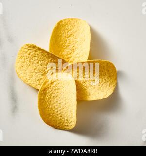 Quatre chips de pomme de terre en forme de fleur sur fond de marbre blanc. Photo de nourriture minimaliste. Banque D'Images