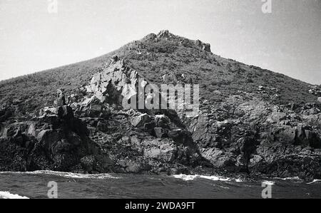 années 1960, historique, vue sur une côte rocheuse de cornouailles avec une colline derrière. La côte de Cornwall est connue pour ses paysages accidentés et granitiques. Banque D'Images