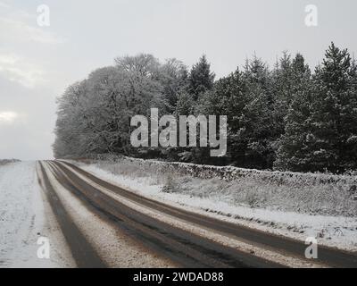 Une scène de neige hivernale dans le nord de l'Angleterre avec une route partiellement couverte par la neige et l'asphalte culminant à travers. Banque D'Images