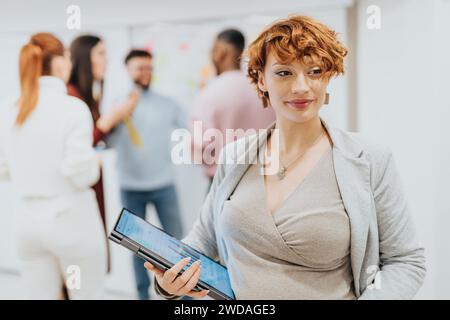 Femme d'affaires enceinte tenant un ordinateur portable. Portrait de femme d'affaires. Les gens qui travaillent à l'arrière. Banque D'Images