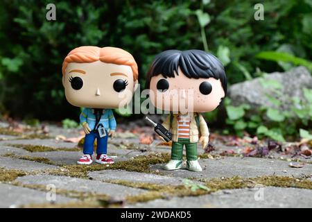 Figurines Funko Pop de Max et Mike de la série télévisée d'horreur populaire Stranger Things. Feuilles vertes, route de pierre mousseline, jardin de printemps. Banque D'Images