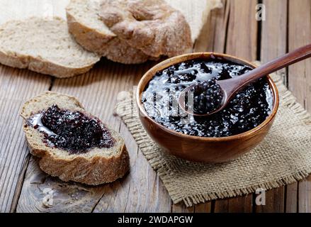 confiture de mûres dans un bol en bois et étalé sur un pain sur fond en bois Banque D'Images