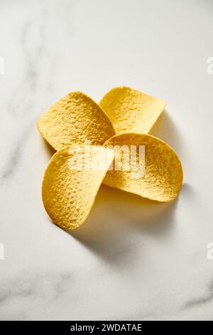 Quatre chips de pomme de terre en forme de fleur sur fond de marbre blanc. Photo de nourriture minimaliste. Banque D'Images