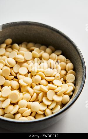 Gouttes de chocolat blanc dans le bol sur fond de marbre blanc. Ingrédient de cuisson Banque D'Images