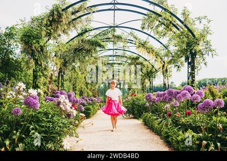 Adorable petite fille jouant dans un beau jardin fleuri par une belle journée ensoleillée, portant un chemisier blanc et une jupe tutu rose vif. Allée avec alliu géant Banque D'Images
