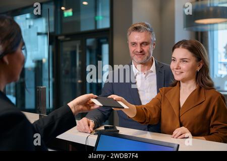 Femme donnant passeport à la réceptionniste près de l'homme à la réception dans l'hôtel Banque D'Images