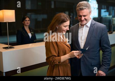 Femme montrant le passeport ouvert à l'homme à la réception dans le hall de l'hôtel Banque D'Images