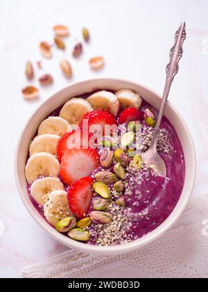 Vue aérienne d'un bol de smoothie végétalien aux baies sain recouvert de banane, fraise, pistaches et graines de chanvre ; espace de copie Banque D'Images