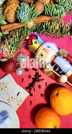 Mise en page de Noël du nouvel an avec des branches d'épinette verte reposant sur un fond rouge, casse-noisette, oranges, noix, épices de vacances, une tasse avec des serviettes sur whi Banque D'Images