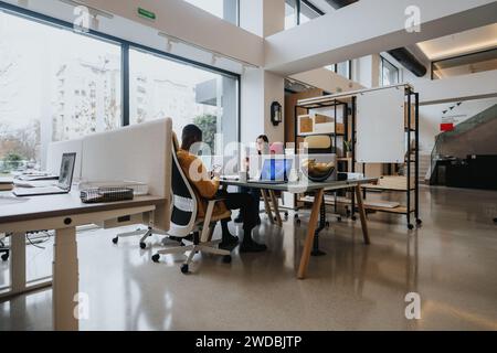 Un groupe multiracial d’employés collabore autour d’une table dans un espace de bureau bien éclairé, mettant en valeur l’accessibilité en fauteuil roulant et le travail d’équipe. Banque D'Images