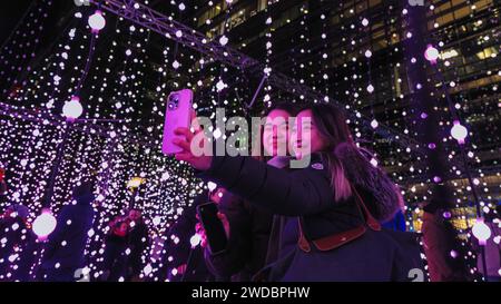 Londres, Royaume-Uni. 19 janvier 2024. Deux visiteurs prennent des photos de « Submergence » de Squidsoup (Royaume-Uni) à Montgomery Square, qui est de retour à la demande populaire après son succès aux Winter Lights en 20219. Les « Winter Lights » annuelles sont spectaculaires et permettent de voir gratuitement des installations lumineuses et de l'art immersif autour de Canary Wharf dans l'est de Londres. Crédit : Imageplotter/Alamy Live News Banque D'Images