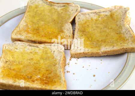 Une photo de morceaux de pain grillé avec du beurre sur une assiette blanche sur un bureau. Banque D'Images