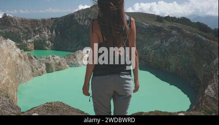 Femme touristique lève les mains au-dessus des lacs de cratère bleu volcanique de Kelimutu. Arrière-plan de la nature. Destination du voyage. Beau paysage sauvage. Vacances d'été exotiques, randonnée, détente. Banque D'Images