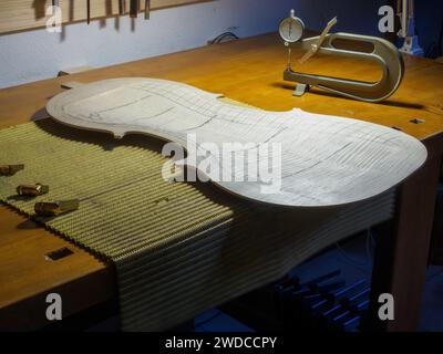 Un établi d'un maître luthier de fabricant d'instruments à cordes montrant un travail en cours de violoncelle plaque arrière, des avions, un calibre d'épaisseur et Banque D'Images