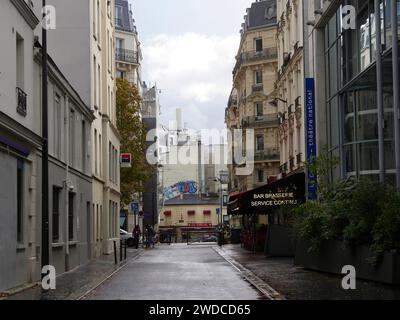 Vue sur une rue humide bordée de bâtiments et un panneau de bar dans une ville, 20e arrondissement, Paris Banque D'Images