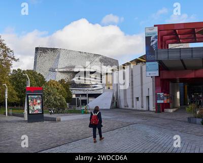 Un homme se tient sur une place devant un bâtiment moderne à la façade saisissante sous un ciel bleu, la Philharmonie de Paris. Paris Banque D'Images