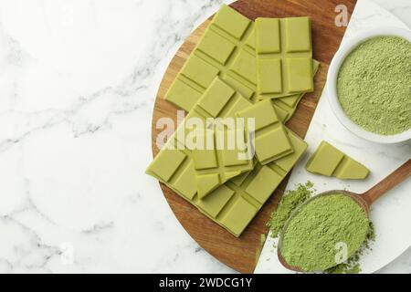 Morceaux de savoureuse barre de chocolat matcha et poudre sur table en marbre blanc, vue de dessus. Espace pour le texte Banque D'Images