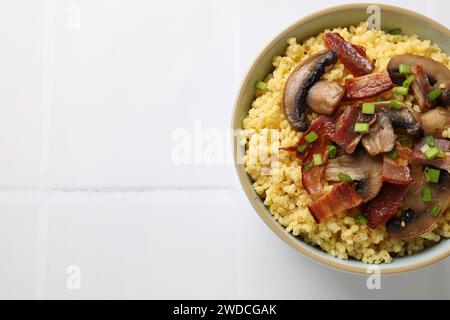 Savoureux porridge de millet avec champignons, bacon et oignon vert dans un bol sur une table carrelée blanche, vue de dessus. Espace pour le texte Banque D'Images