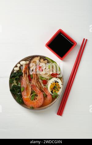 Délicieux ramen avec crevettes et œuf dans un bol servi sur une table en bois blanc, plat. Soupe de nouilles Banque D'Images