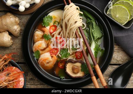 Composition de pose plate avec de délicieux ramen dans un bol et des ingrédients sur une table en bois. Soupe de nouilles Banque D'Images