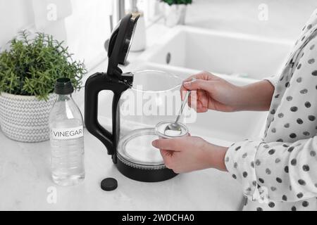 Femme ajoutant du bicarbonate de soude dans une bouilloire électrique dans la cuisine, closeup Banque D'Images