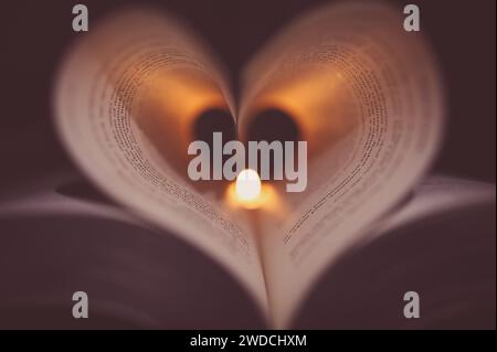 Heart on Fire - pages de livres moulées pour ressembler à un cœur avec une bougie chauffe-plat illuminant les pages projetant des ombres sur les mots. Banque D'Images