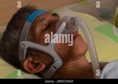 Un homme asiatique ou endormi avec une machine de CPAP pour le traitement de l'apnée du sommeil dans un cadre domestique Banque D'Images