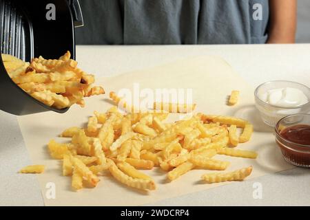 Versez sur la table les morceaux de pommes de terre ondulées du plateau de l'airfryer. Cuisson des frites à l'aide de la friteuse à air Banque D'Images