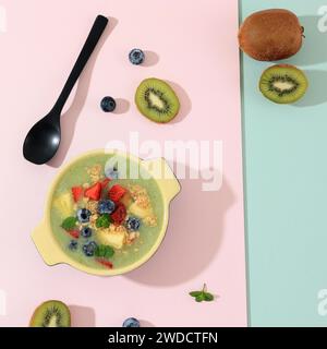 Vue de dessus Green Kiwi Smoothie avec garniture aux fraises, granola et bleuets, sur fond rose Banque D'Images