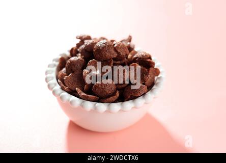 Céréales au chocolat Crunchy croustillant au cacao dans un bol blanc. Flocons de maïs aromatisés au chocolat. Sur fond rose. Blé. Banque D'Images