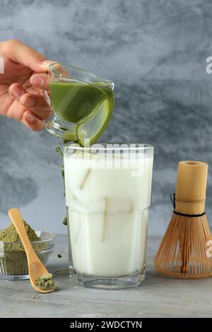 Verser le Matcha vert dans le verre avec du lait et de la glace, sur fond gris Banque D'Images